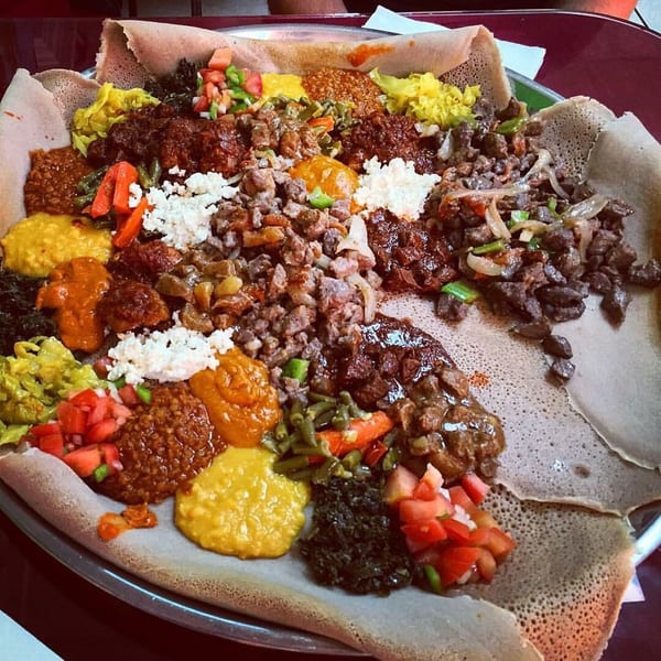 A large platter of Ethiopian injera bread topped with various colorful stews, meats, and vegetables.