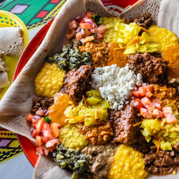 Colorful Ethiopian injera platter with various stews, vegetables, and cheese, with rolled injera on the side.
