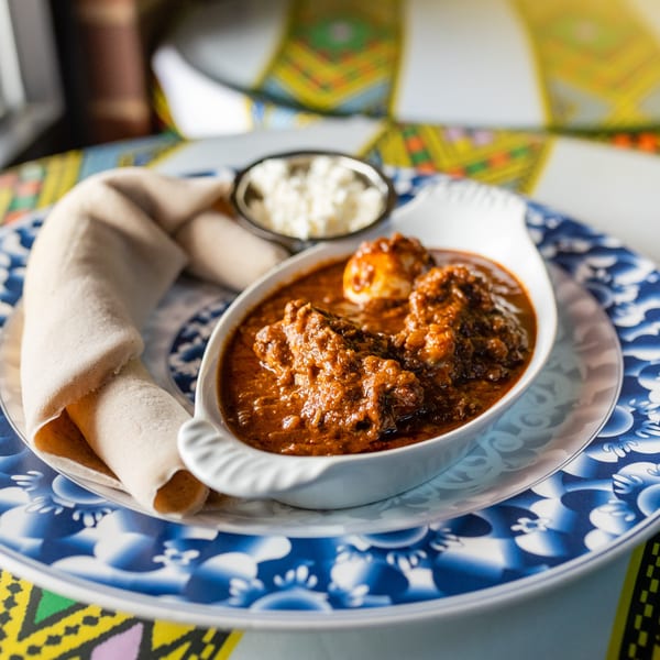 Doro Wat, an Ethiopian chicken stew, with injera bread and a side of cheese on a blue patterned plate.