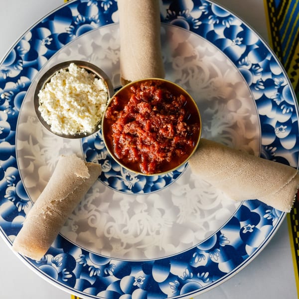 Overhead view of injera rolls, red stew, and white cheese on a blue and white plate.