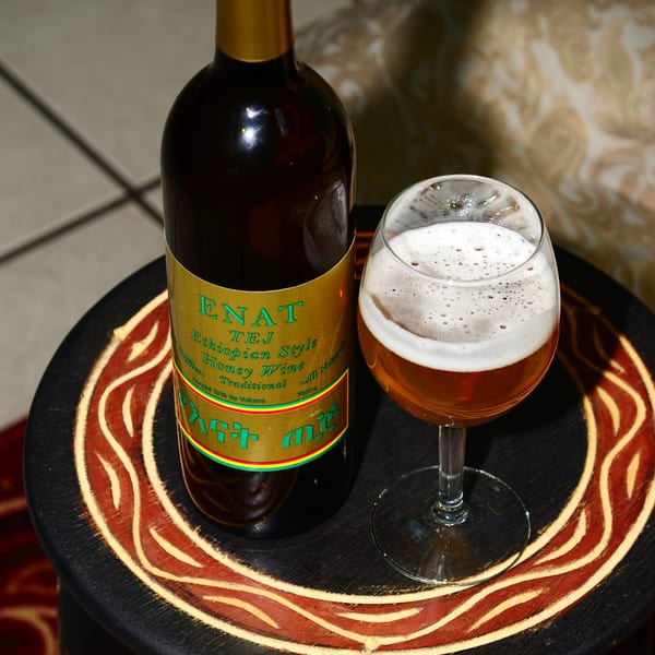 A bottle of Enat Tej Ethiopian honey wine and a glass of the amber-colored wine with foam.