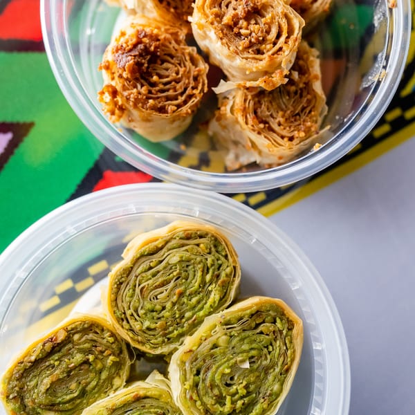 Two plastic containers of rolled baklava, one with pistachio and one with walnuts.