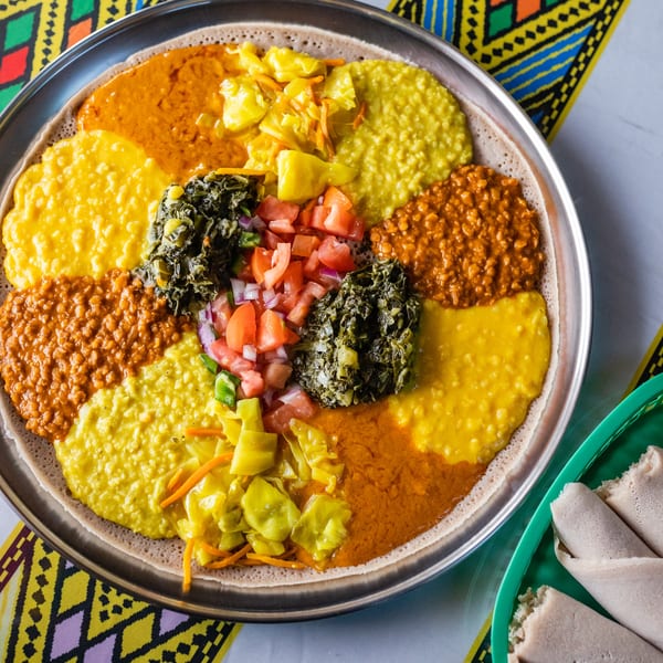 A large platter of colorful Ethiopian food, including injera, stews, and vegetables, on a patterned tablecloth.