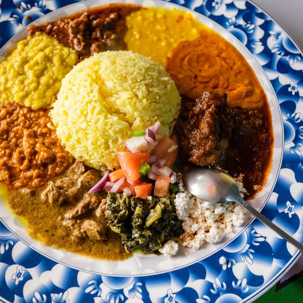 A colorful Ethiopian platter with yellow rice, various stews, vegetables, and cheese on a blue and white plate.